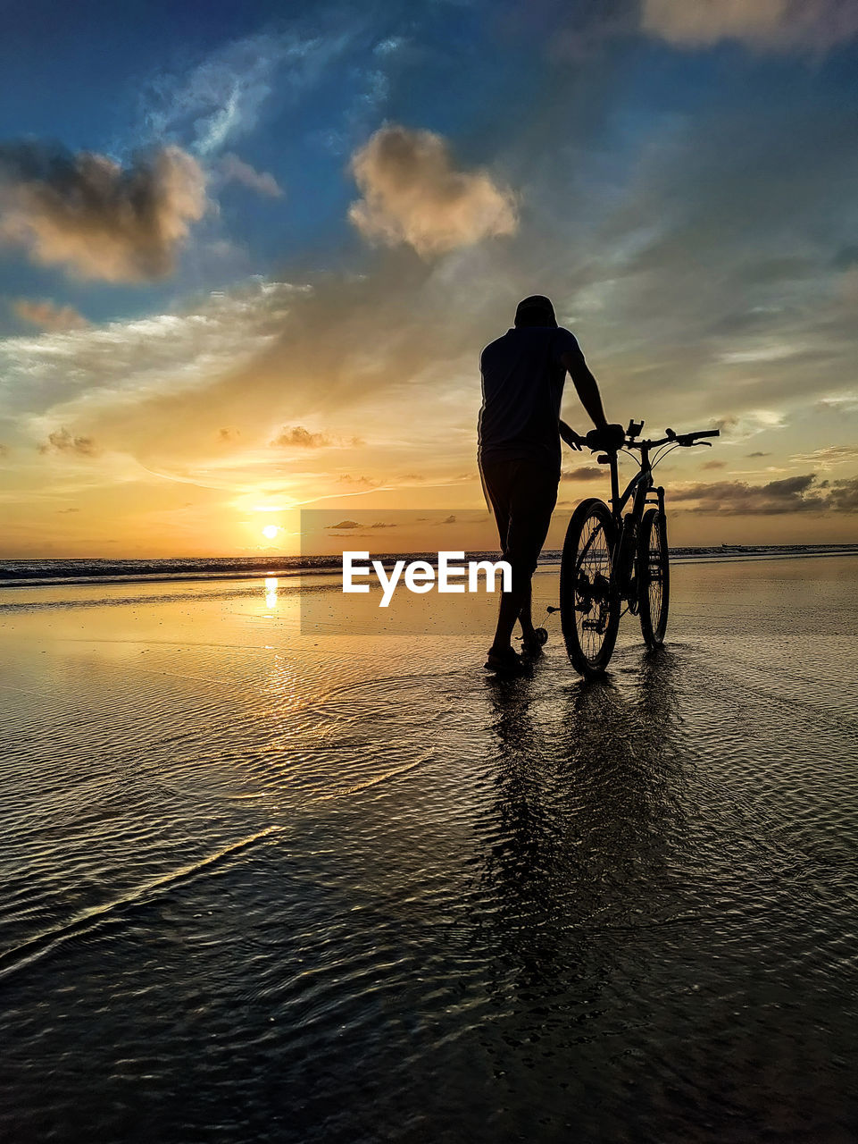 Silhouette man riding bicycle on beach against sky during sunset