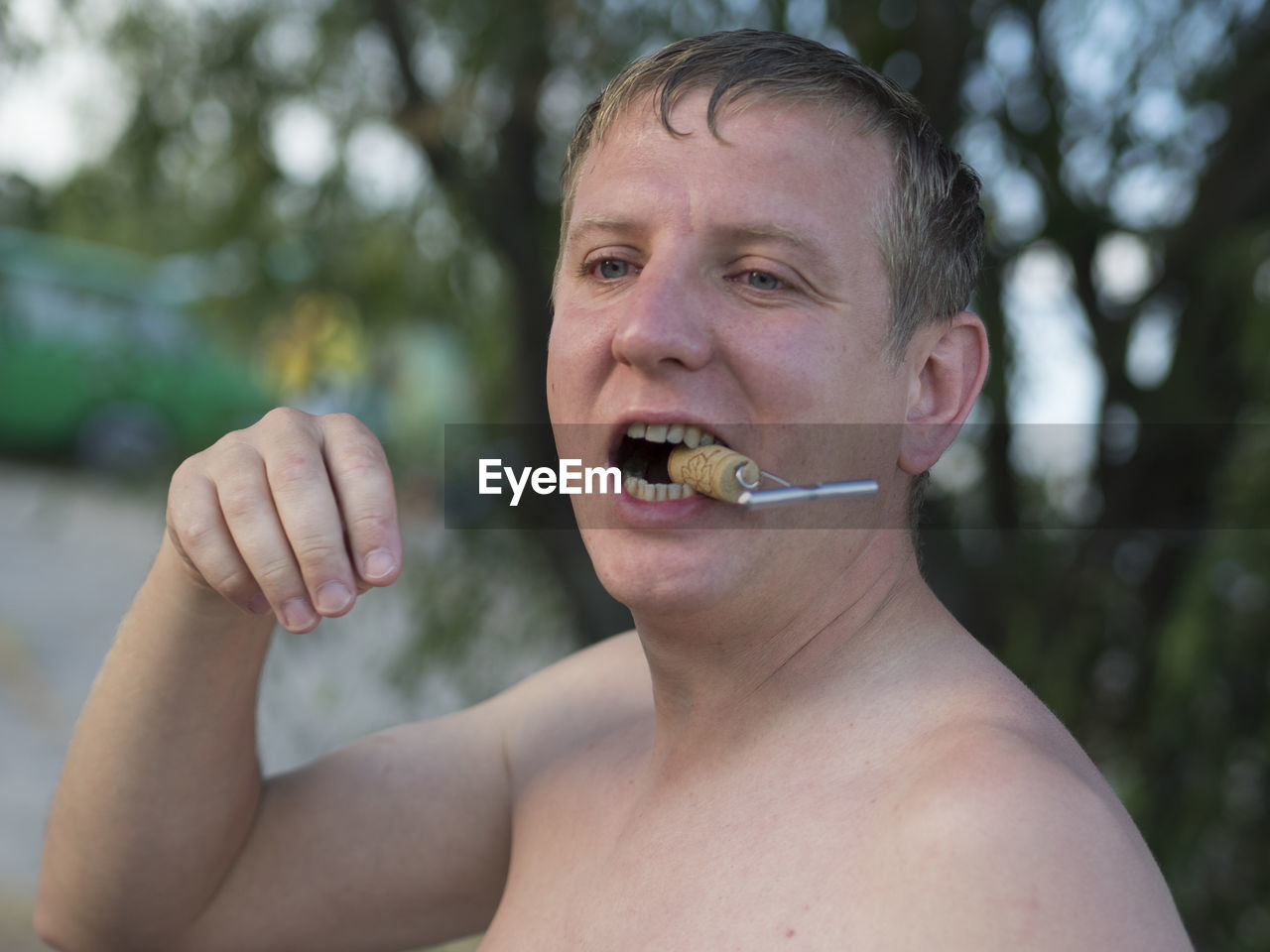 Shirtless man holding cork in mouth