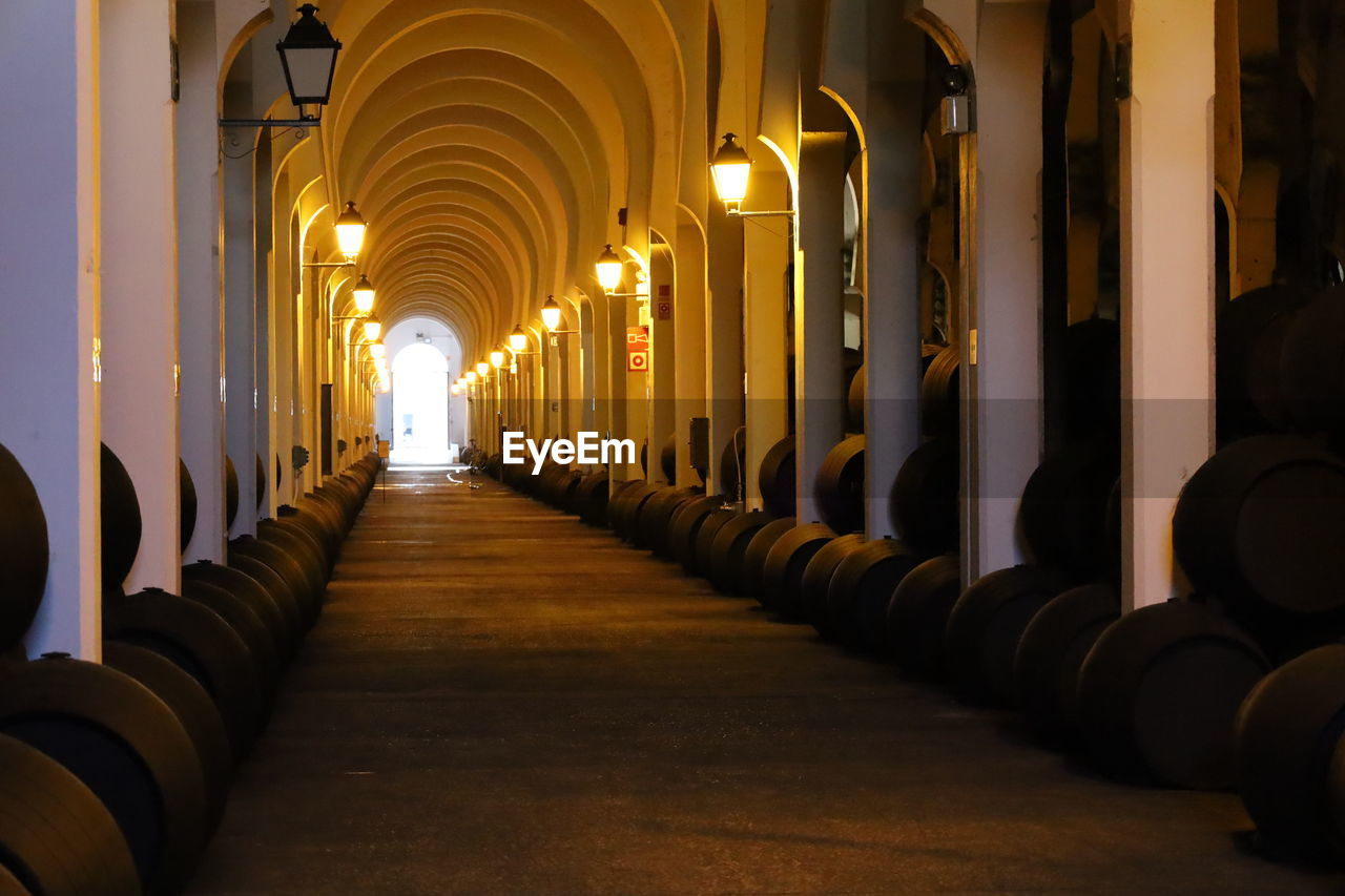 architecture, in a row, arch, building, indoors, built structure, arcade, aisle, corridor, diminishing perspective, architectural column, no people, wine, wine cellar, alcohol, history, light, the past, lighting equipment, the way forward, travel destinations, illuminated, cellar, repetition, drink, religion, hall