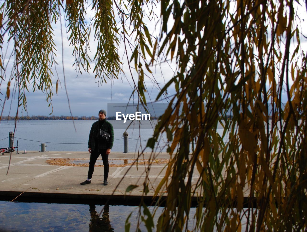 MAN STANDING ON SHORE AGAINST SKY