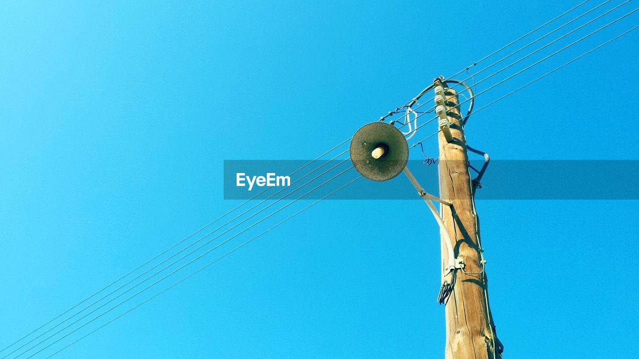 Low angle view of electricity pylon against blue sky