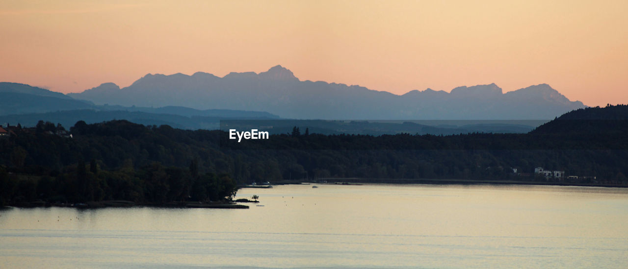 SCENIC VIEW OF LAKE BY SILHOUETTE MOUNTAINS AGAINST SKY DURING SUNSET