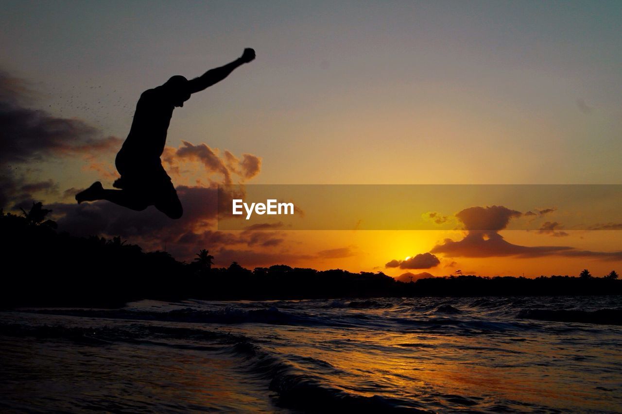 Silhouette man jumping at beach during sunset