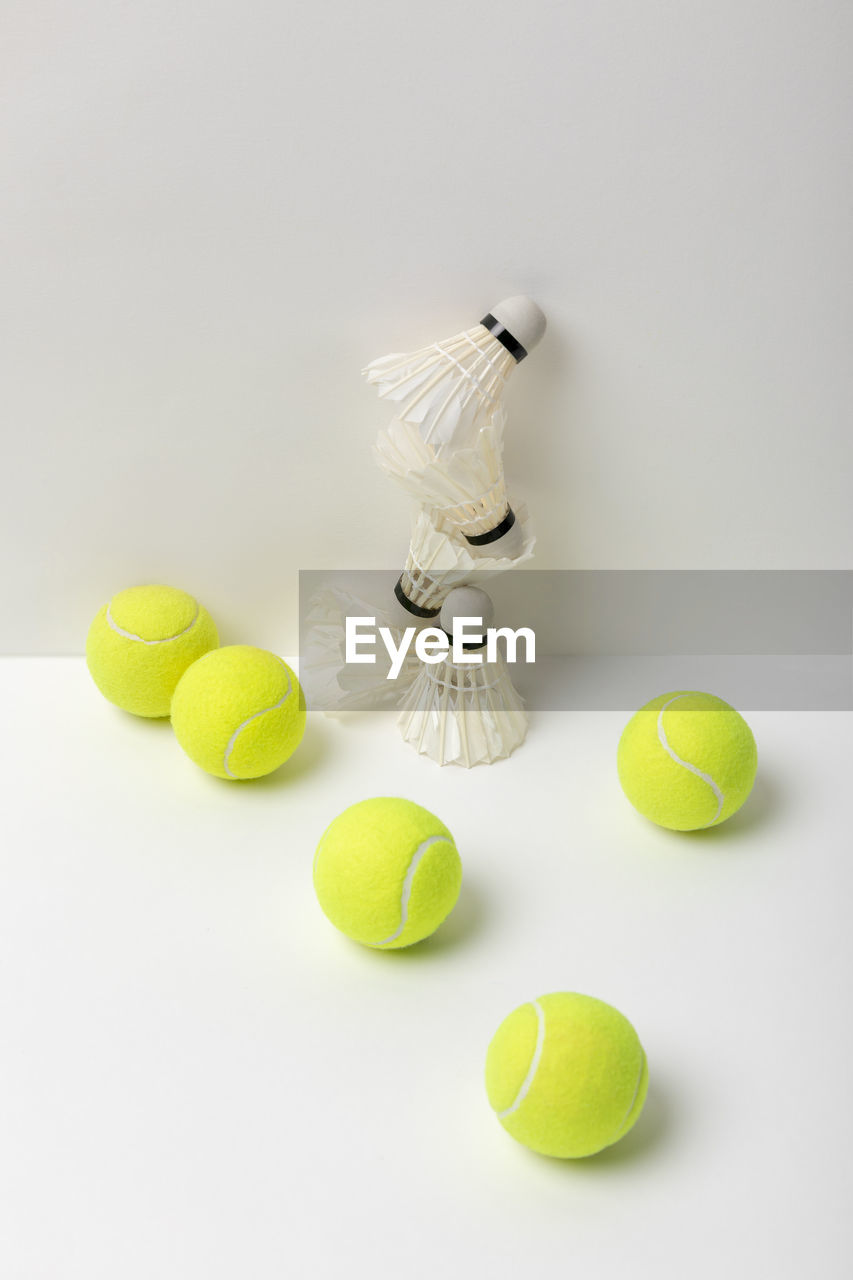 High angle view of tennis ball with shuttle cock against white background