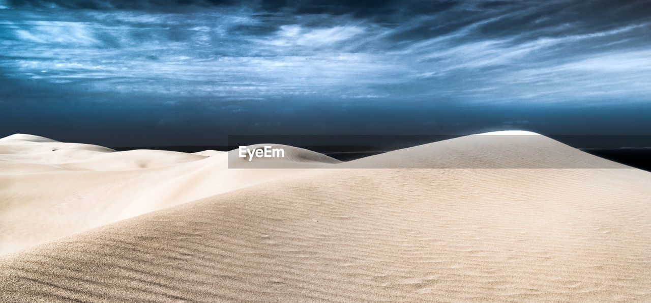 Scenic view of sand dunes at desert against cloudy sky