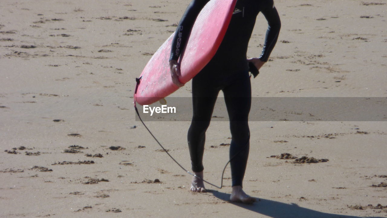 Low angle view of man standing with surfboard on beach