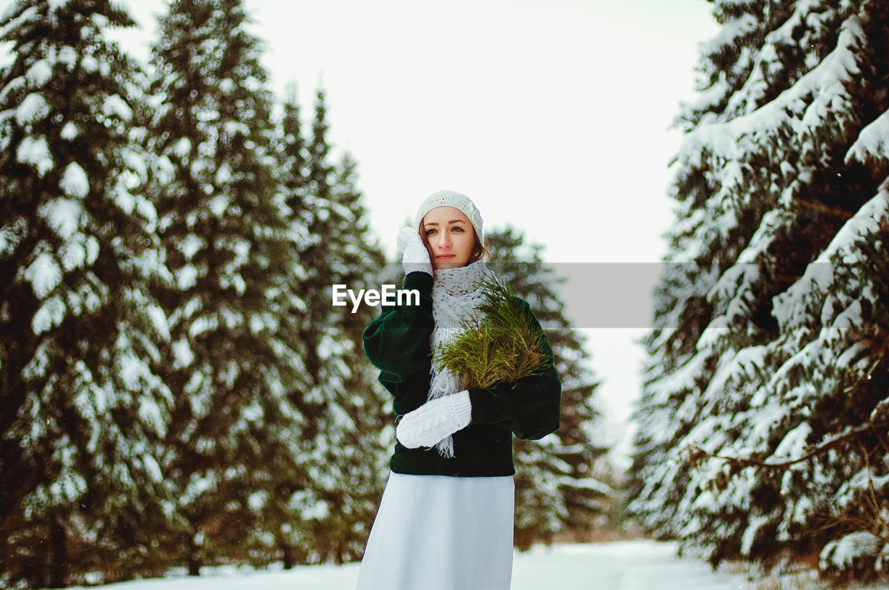 Redhead beautiful woman in green sweater and white gloves walking in the frozen winter forest.