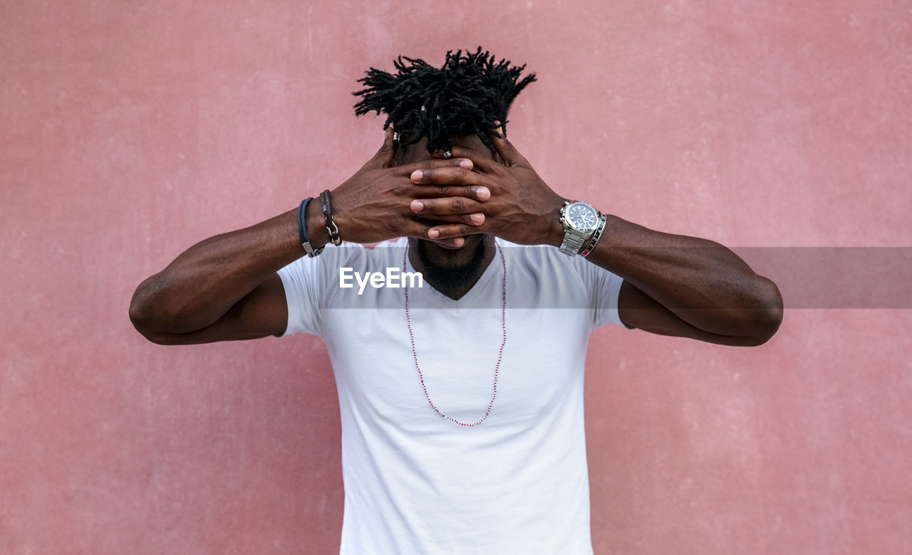 Mid adult man with hands covering eyes while standing against pink wall