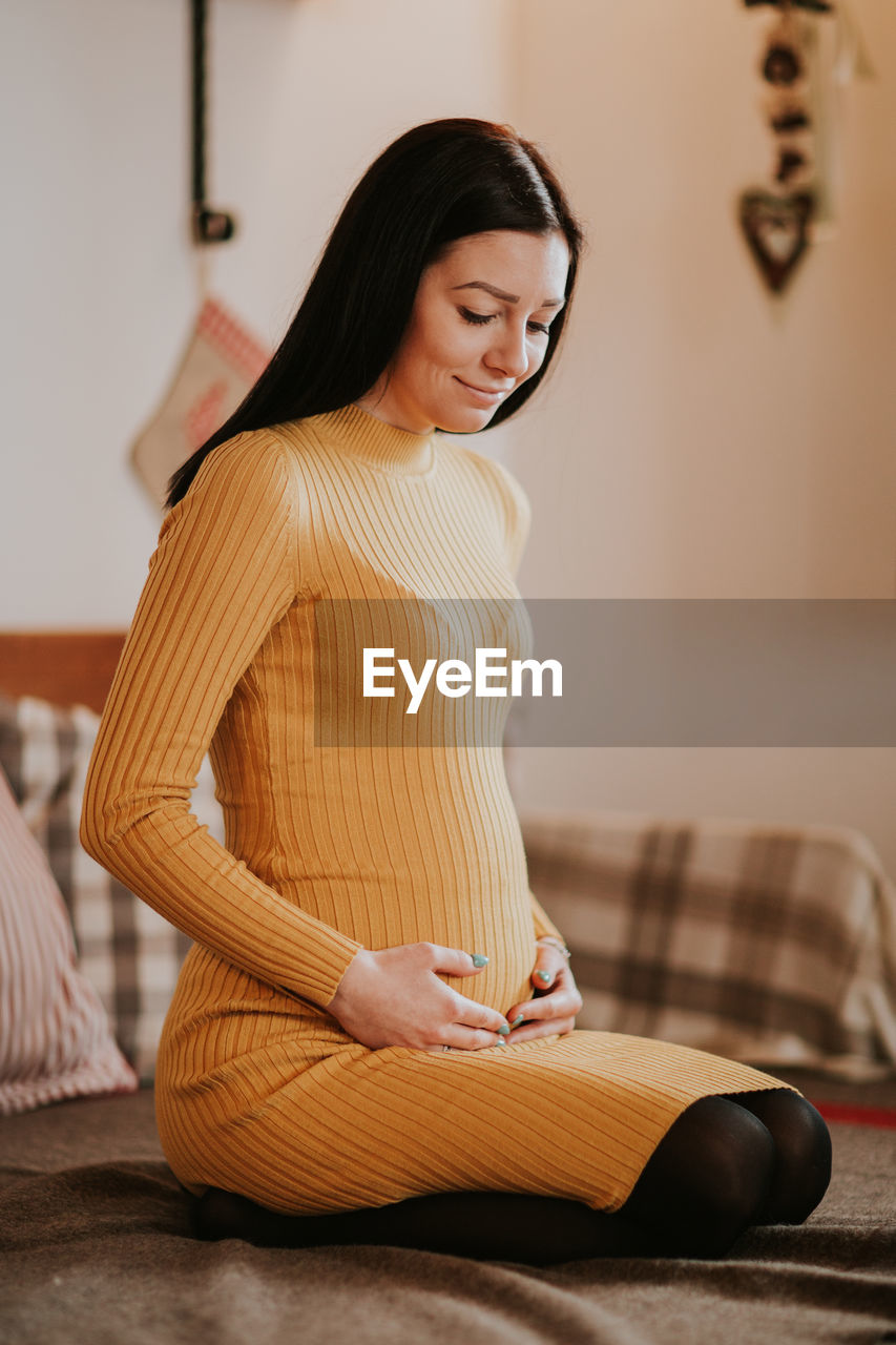 Smiling pregnant woman sitting on bed at home