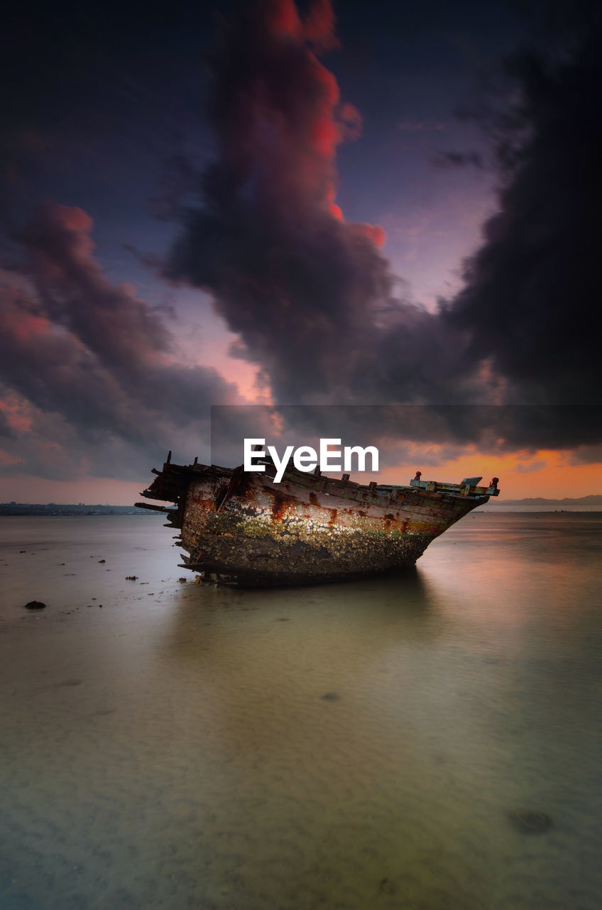 Broken boat against sky at beach during sunset