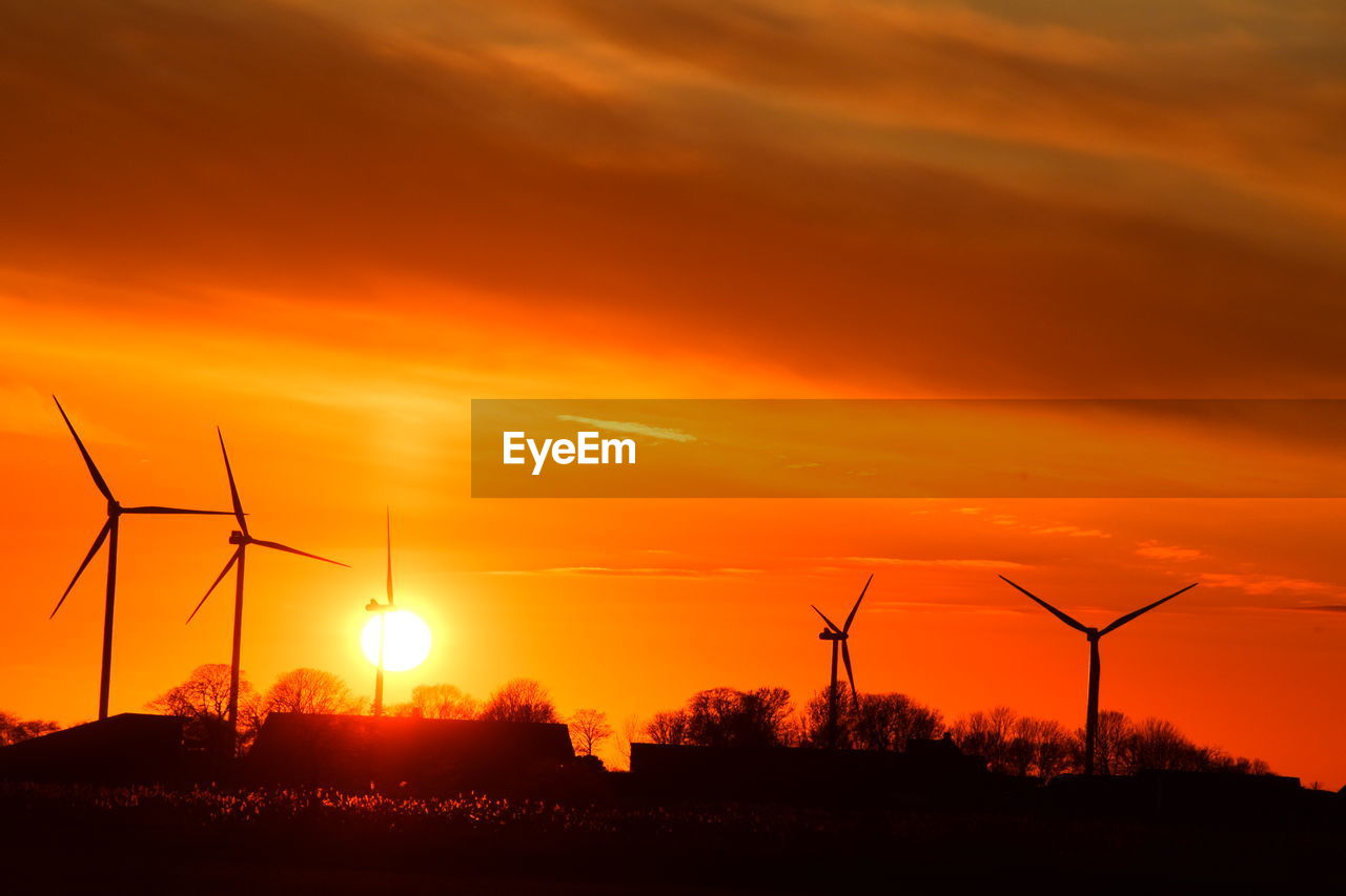 SILHOUETTE OF WIND TURBINES ON FIELD AGAINST ORANGE SKY