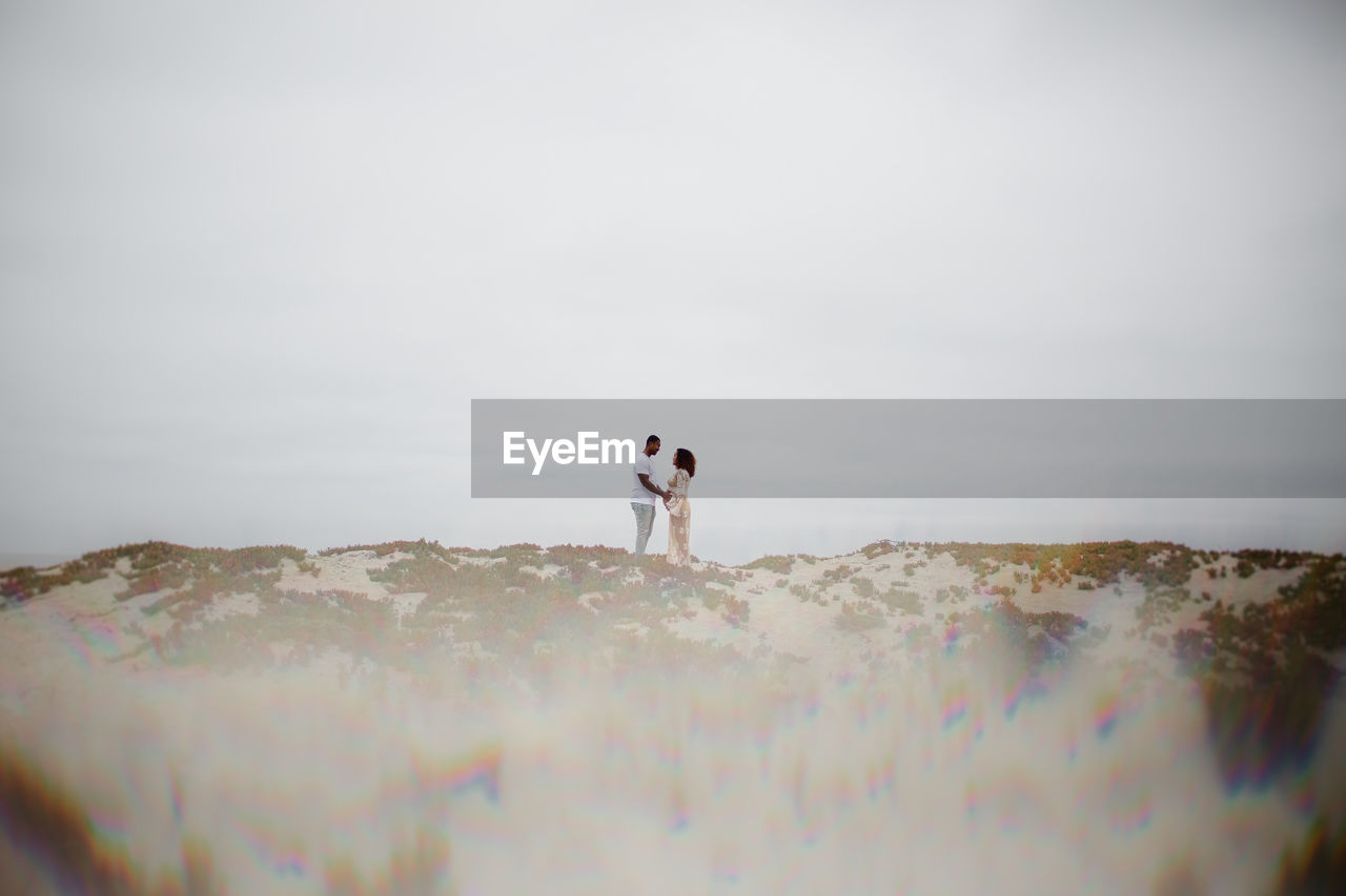 Mixed race couple posing on sand dunes with prism effect