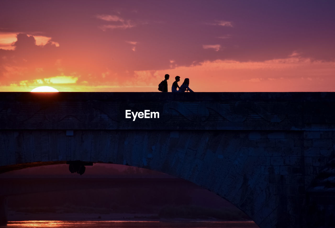 Silhouette of young friends on a colorful sunset when returning home, crossing a bridge.