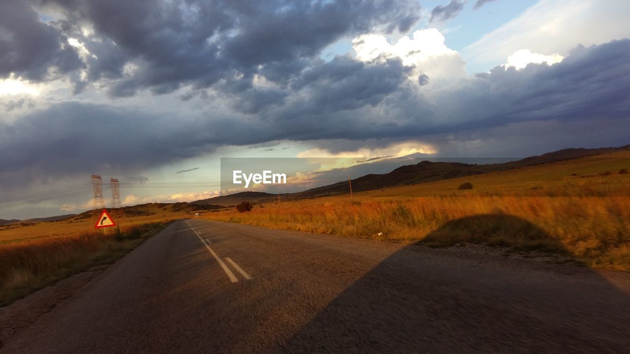 Empty country road against cloudy sky