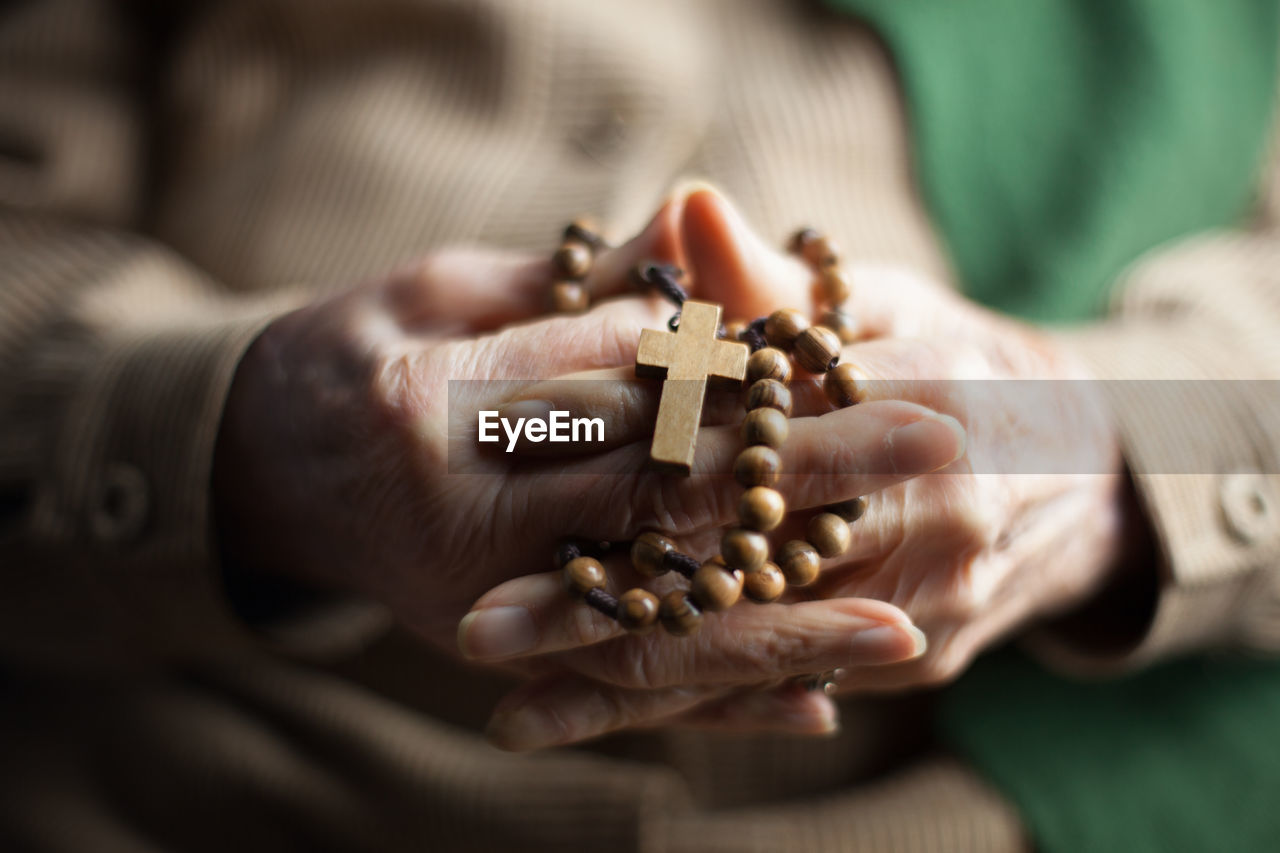 Close-up of woman holding rosary with hands clasped