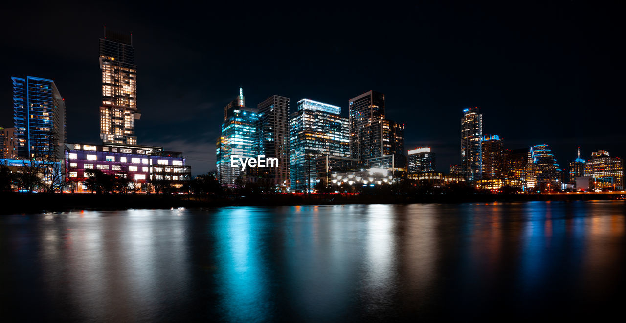 Illuminated buildings by river against sky at night