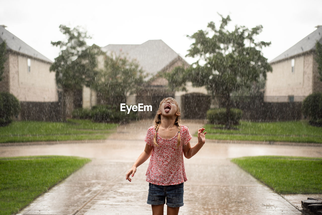 Playful girl with mouth open standing on driveway during rainfall