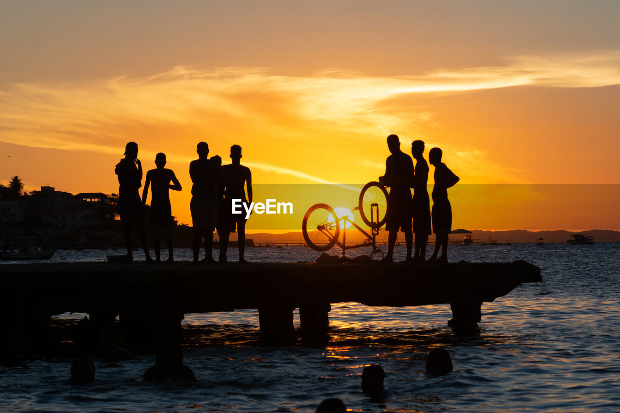 Dozens of young people, in silhouette, are seen on top of the crush bridge having fun. 