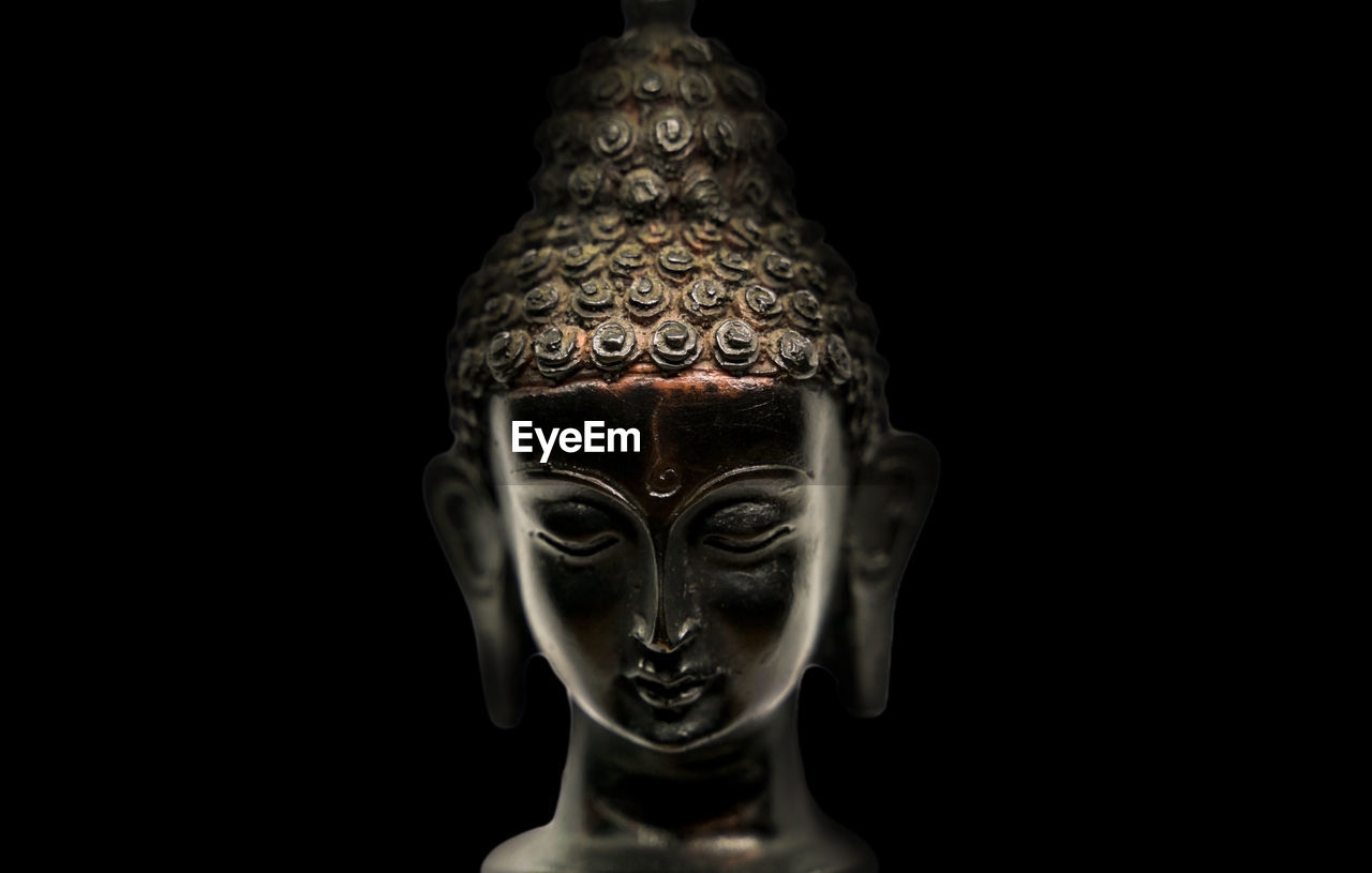 Buddha head black statue in a meditation state with closed eyes isolated on black background.