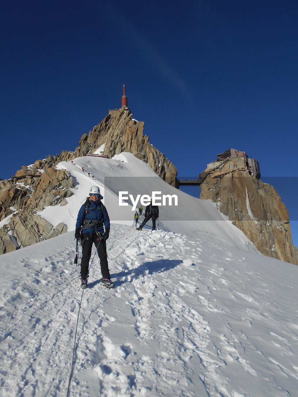 Low angle view of hikers standing at aiguille du midi against blue sky