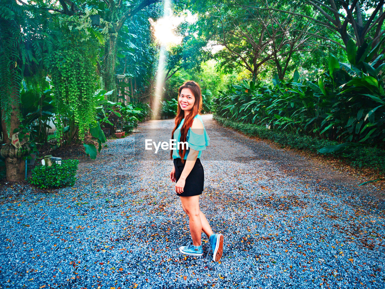 Portrait of mid adult woman standing on footpath amidst plants in park