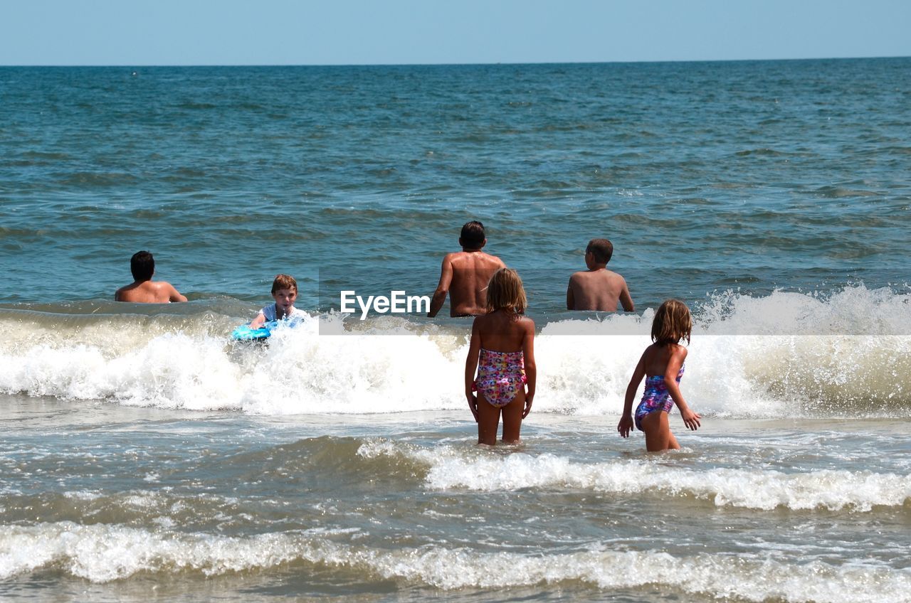 PEOPLE STANDING AT BEACH AGAINST CLEAR SKY