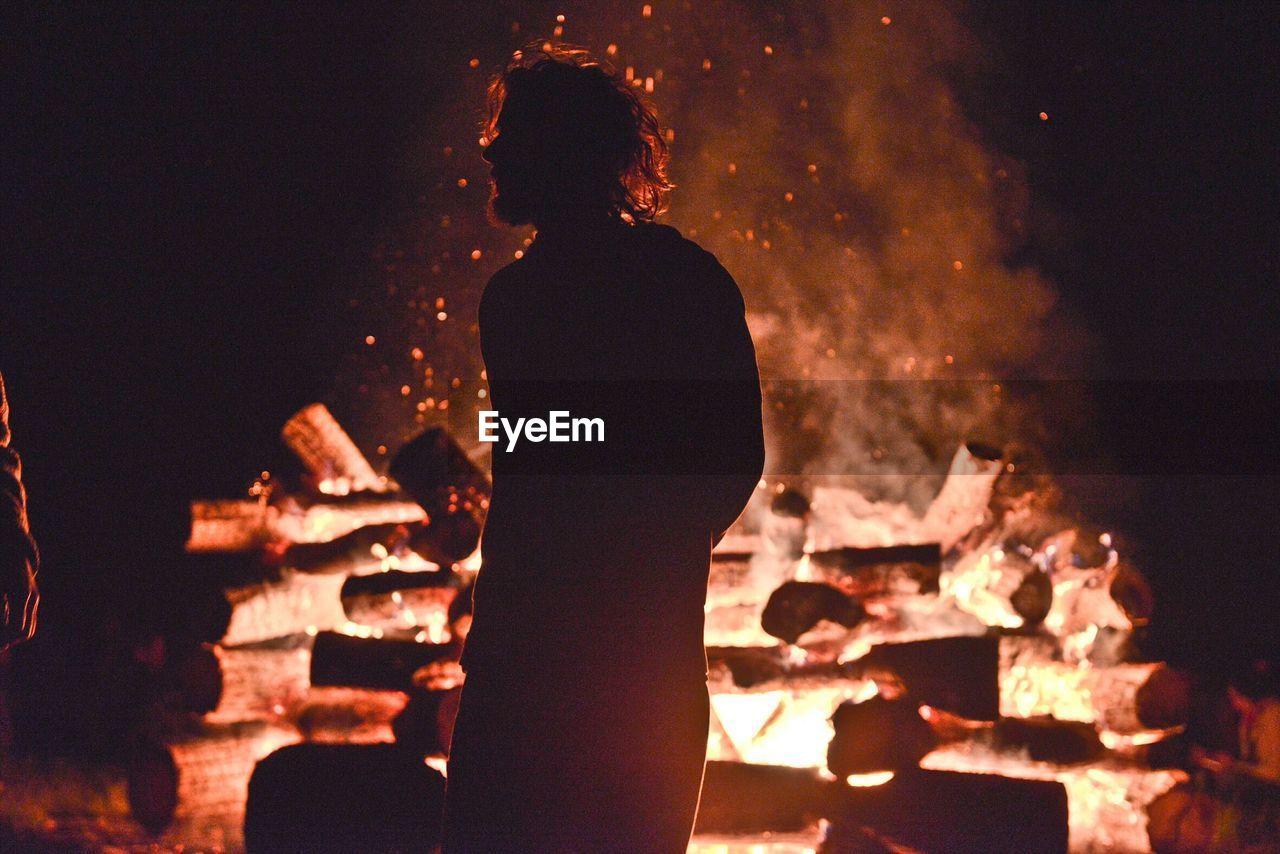 Man standing by bonfire on field at night