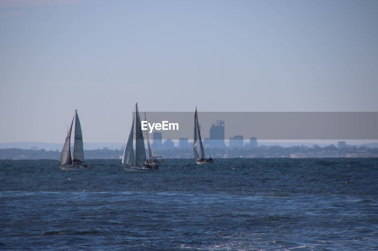 Sailboats sailing in sea against clear sky