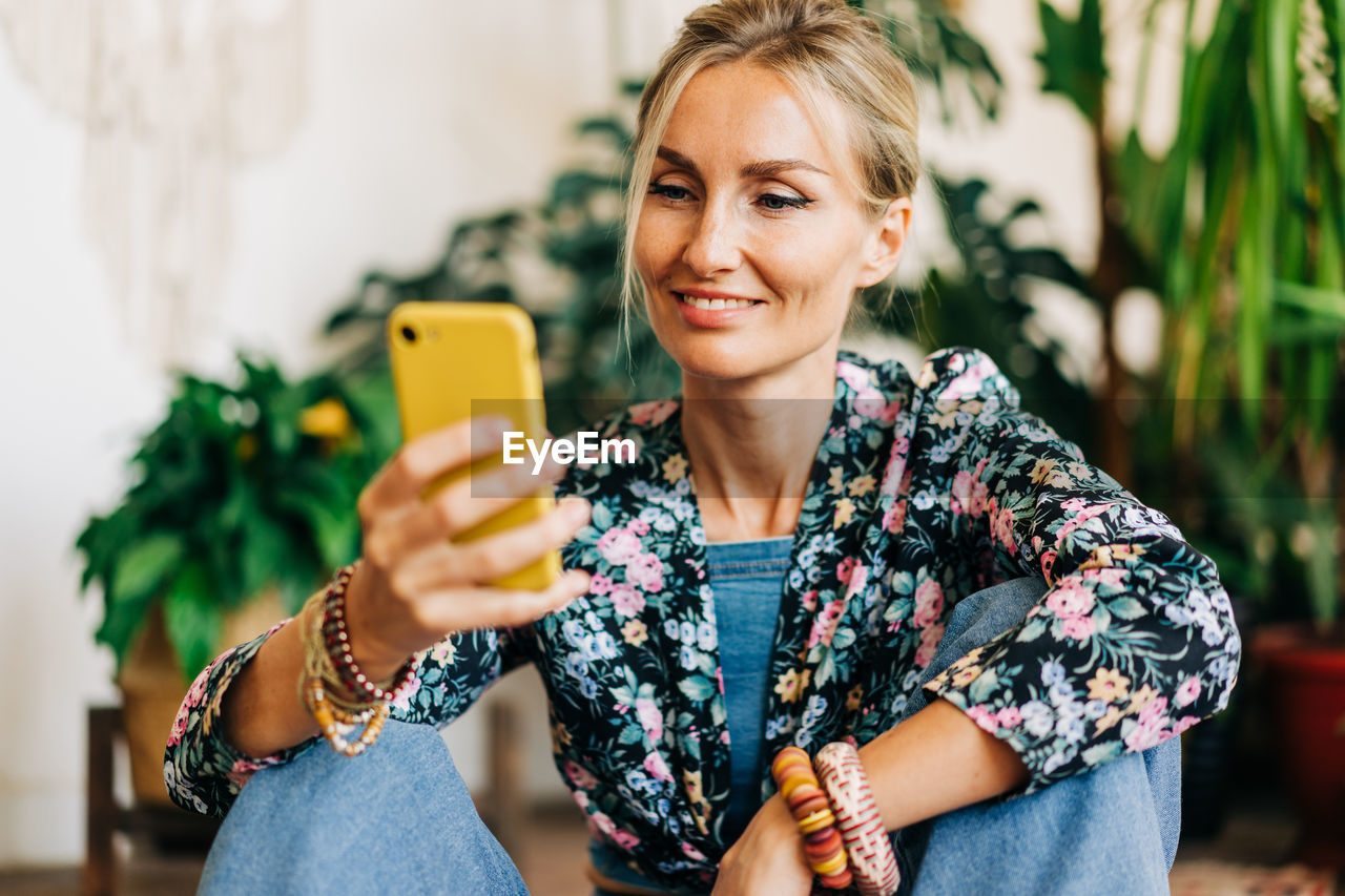 Smiling blonde looks at the screen of a mobile phone and reads a message.