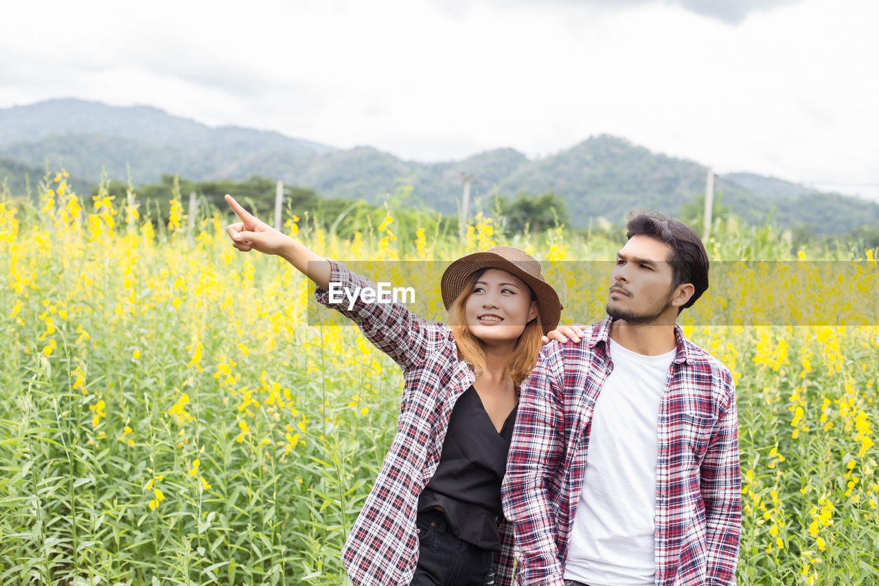 Woman pointing while standing with man by plants against sky