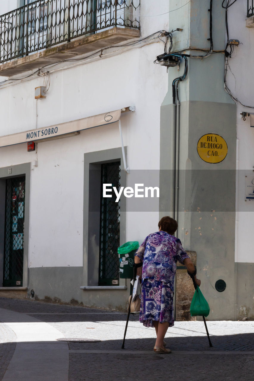 REAR VIEW OF WOMAN WALKING ON STREET AGAINST BUILDING