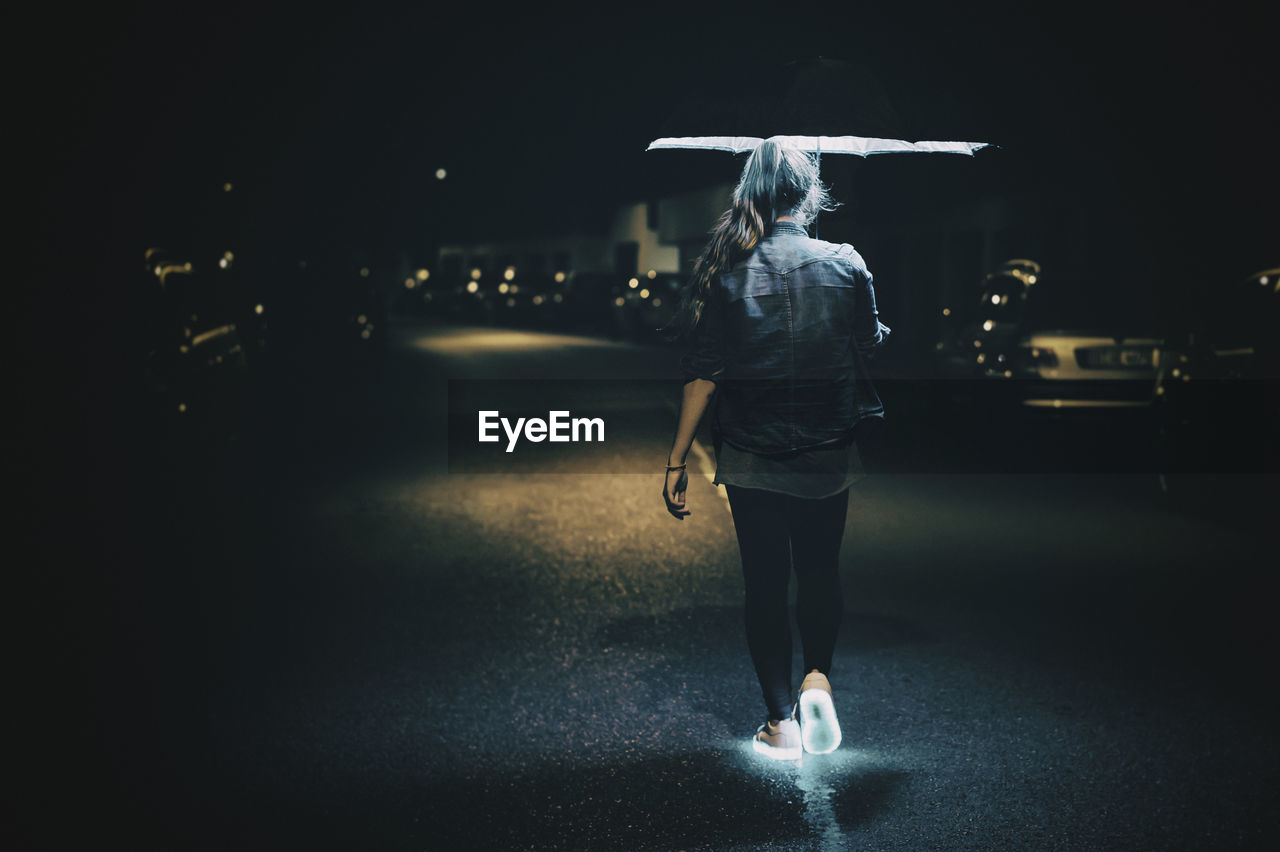 Rear view of woman walking with glowing shoes on street at night