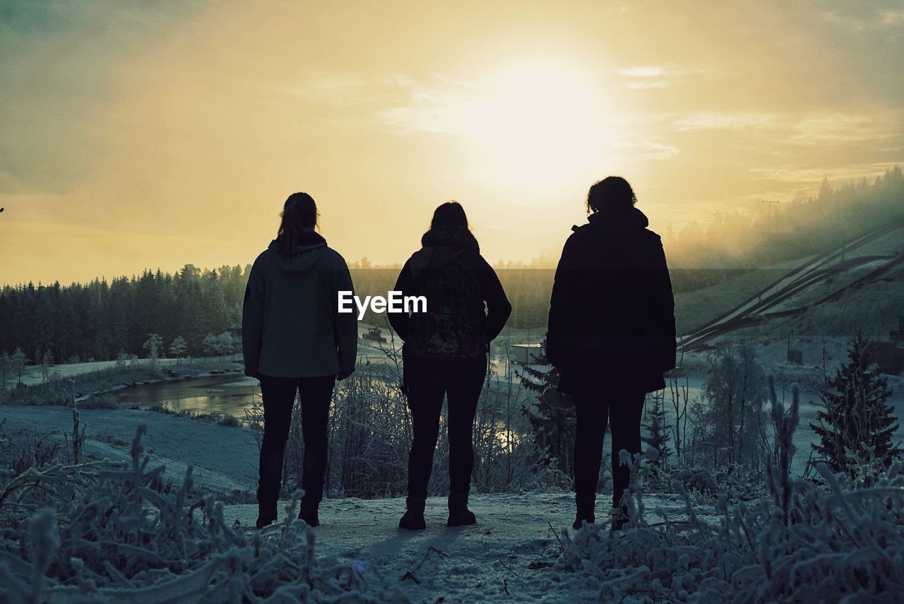 Rear view of people on snow covered landscape during sunset