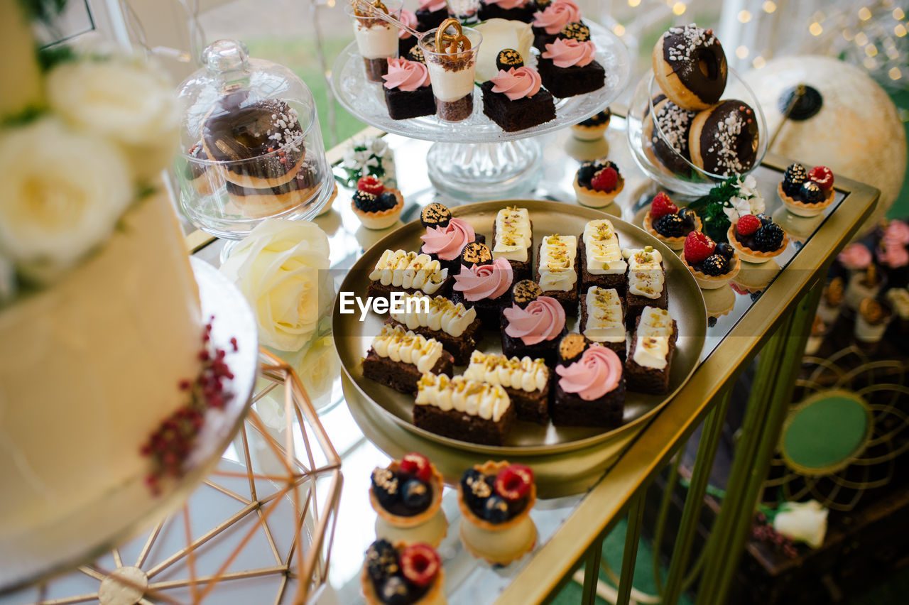 From above sweet delicious creamy chocolate cakes on round tray doughnuts and berry tartlets on festive table in dessert bar in cafe