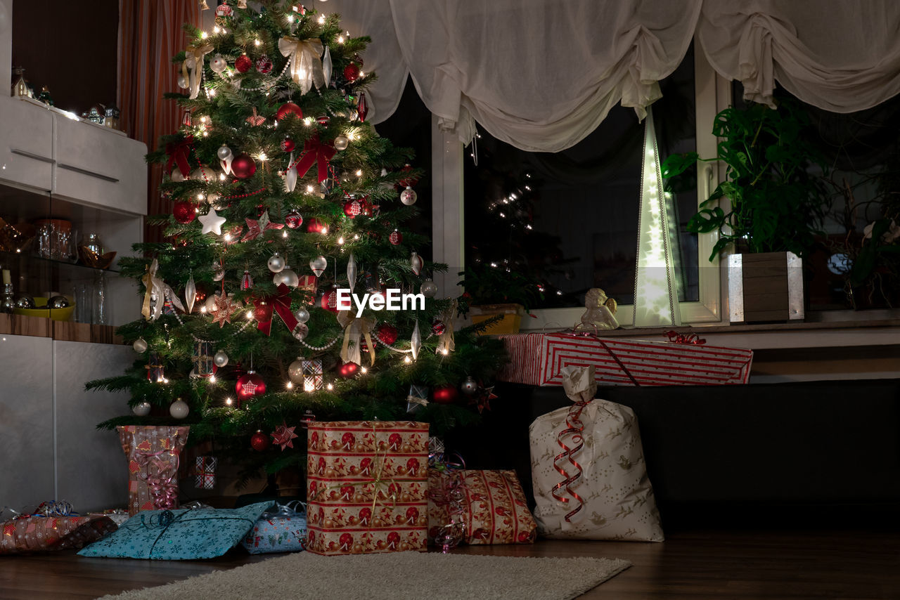 Its christmas eve. the christmas tree is a decorated nordmann fir. many presents are under the tree.