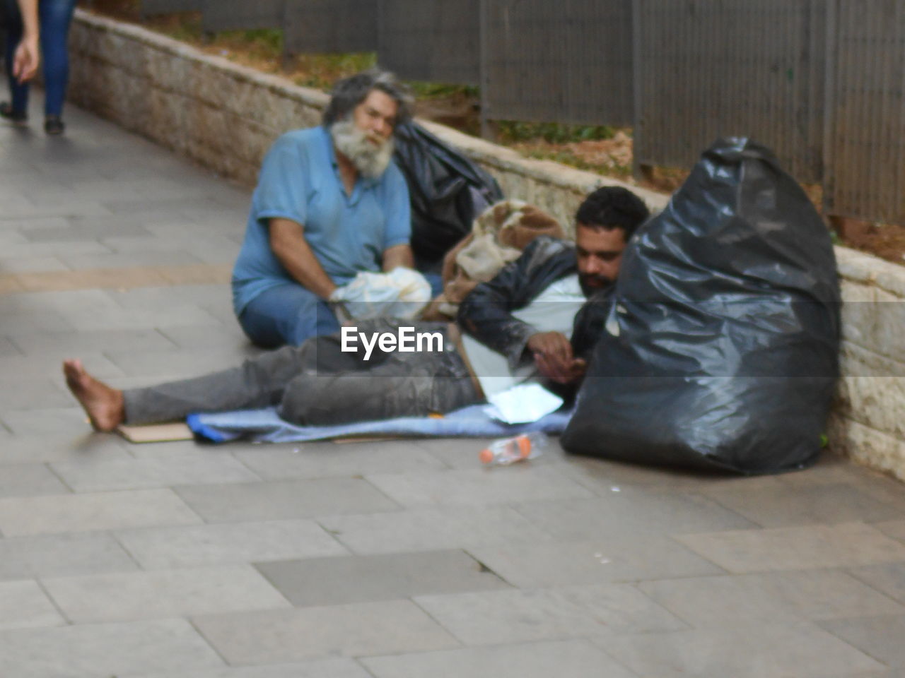 PEOPLE SITTING ON FOOTPATH BY STREET