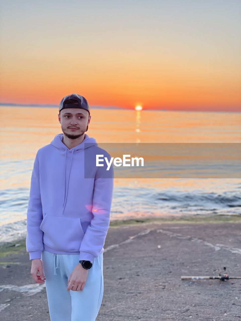 PORTRAIT OF MAN STANDING ON BEACH AGAINST SKY DURING SUNSET