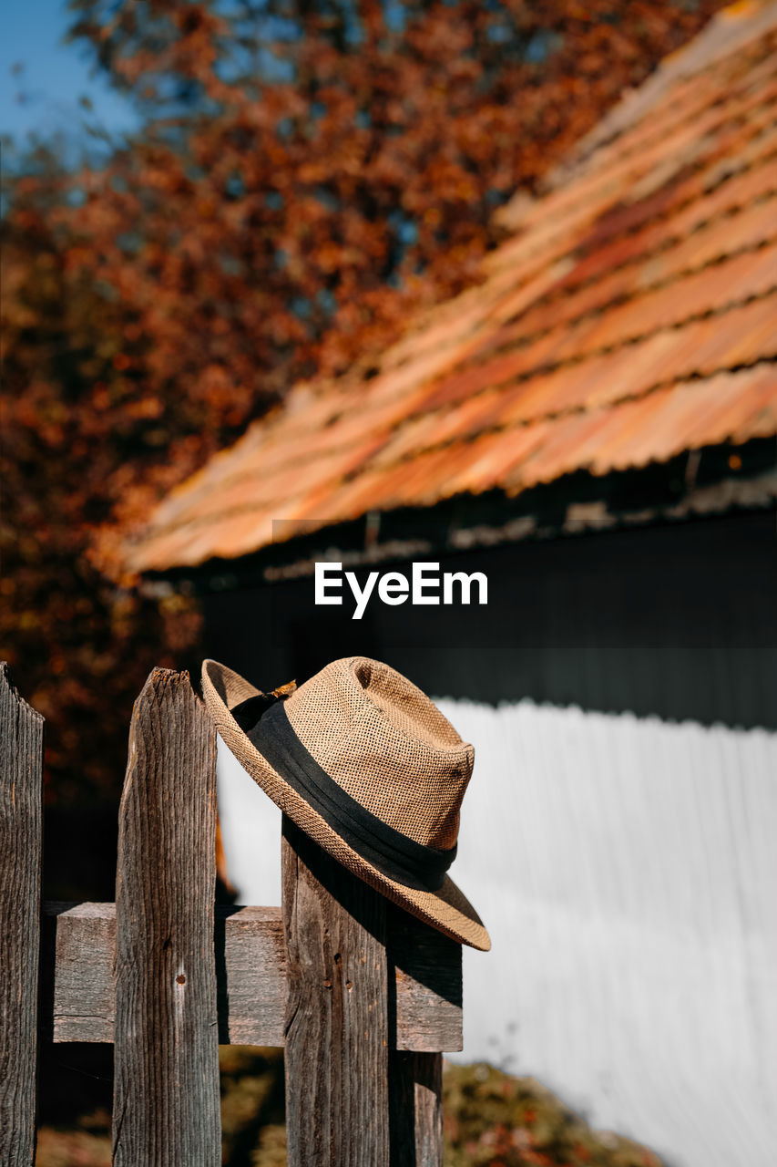 Close-up of wooden fence and hat against rustic house