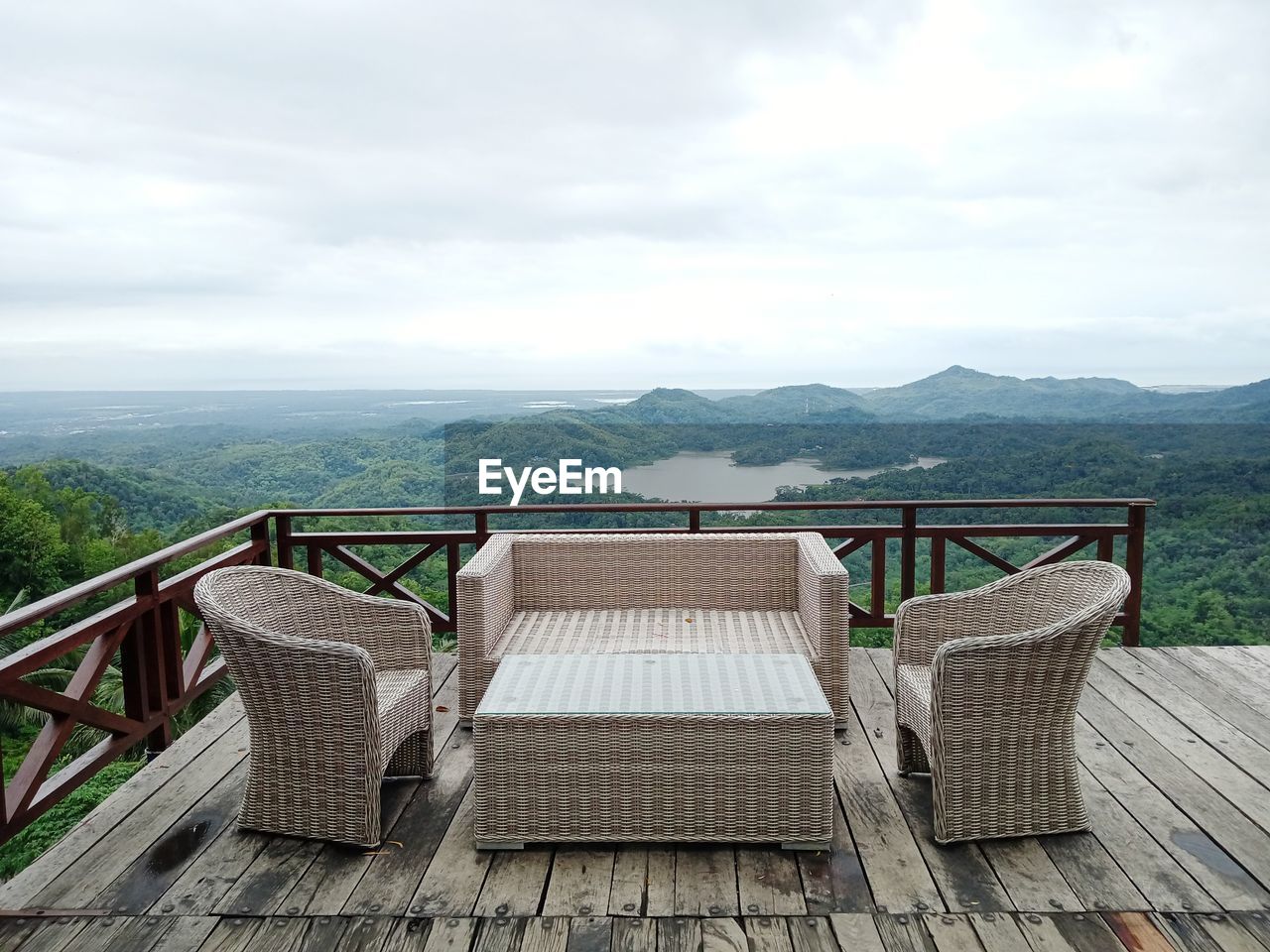 Empty chairs on railing against sky