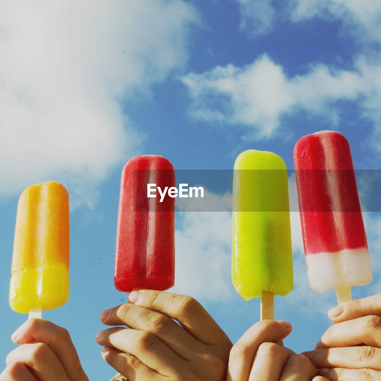 Cropped image of people holding popsicles against cloudy sky