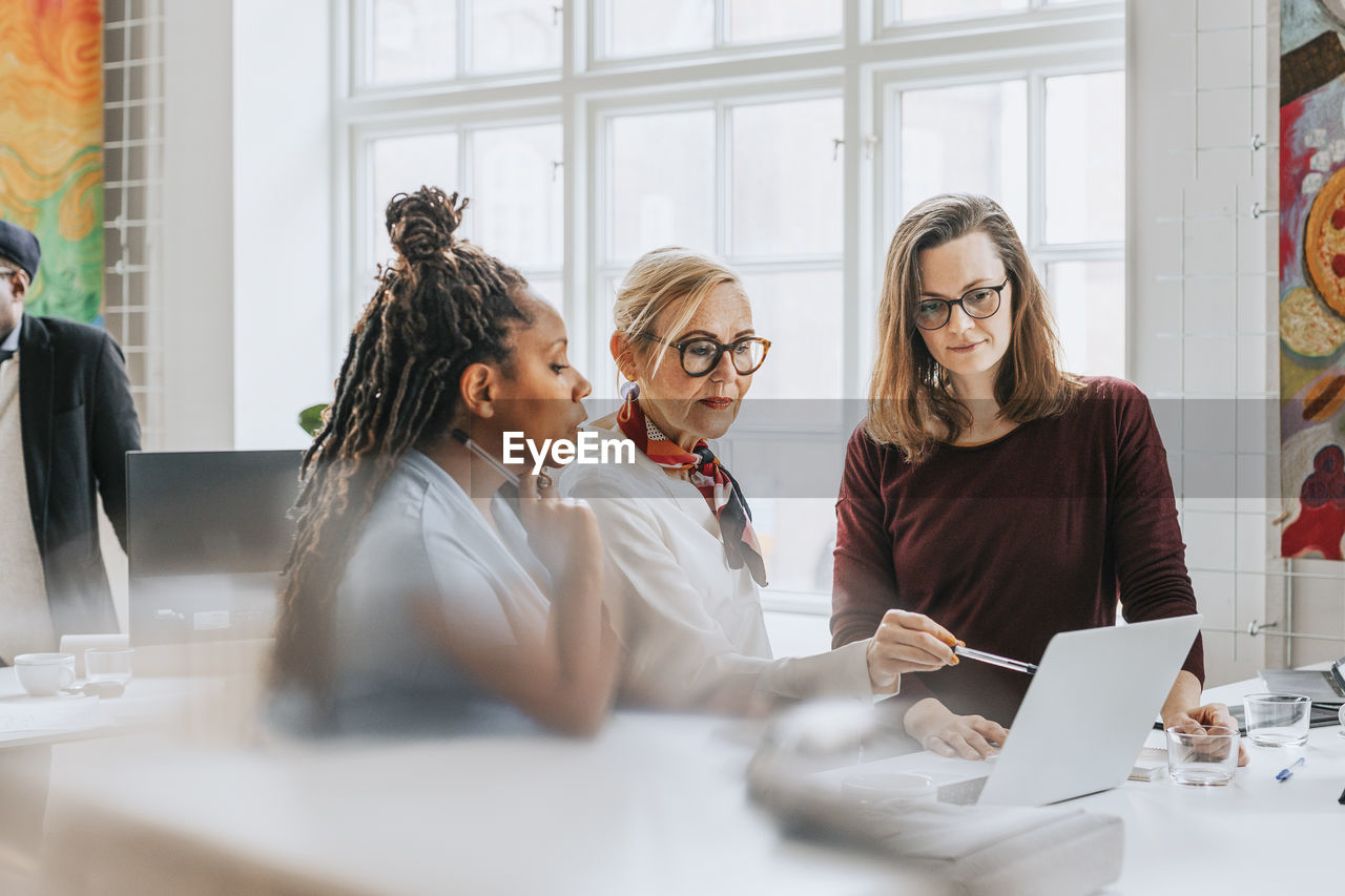 Businesswoman pointing at laptop while discussing with female colleagues at office