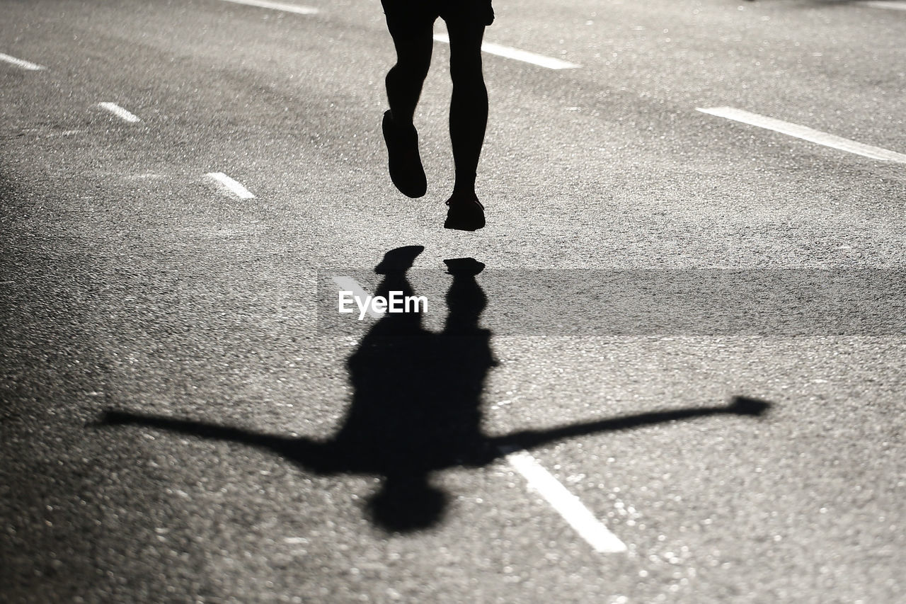 Low section of silhouette man jumping on road during sunny day