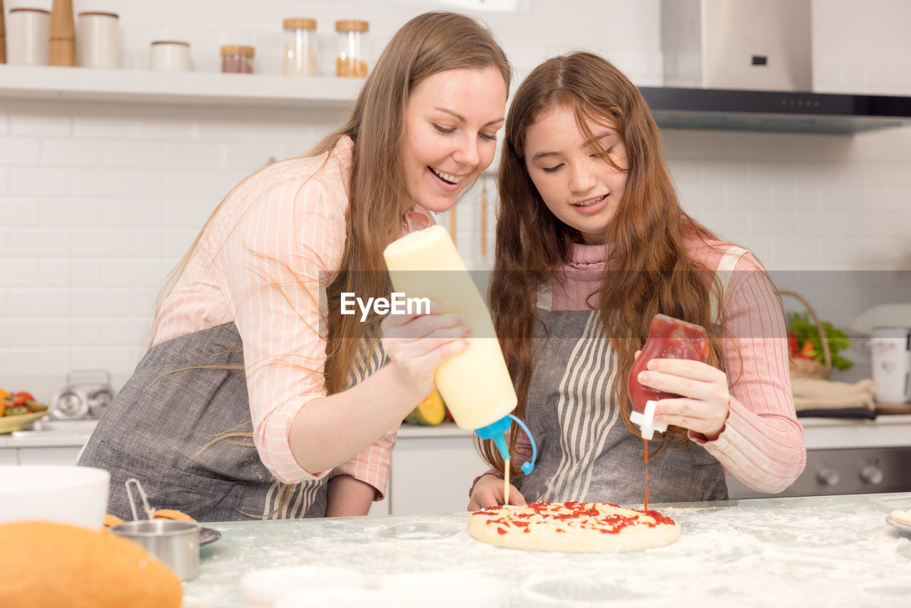 In the kitchen at home, a playful mother and daughter yell while making pizza dough.