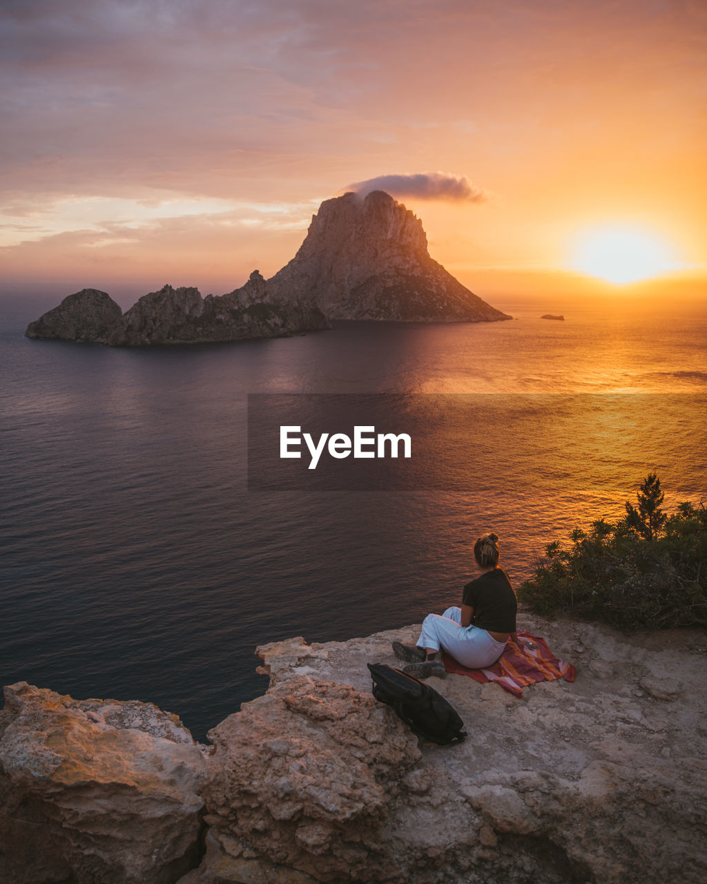 Woman sitting against sea during sunset