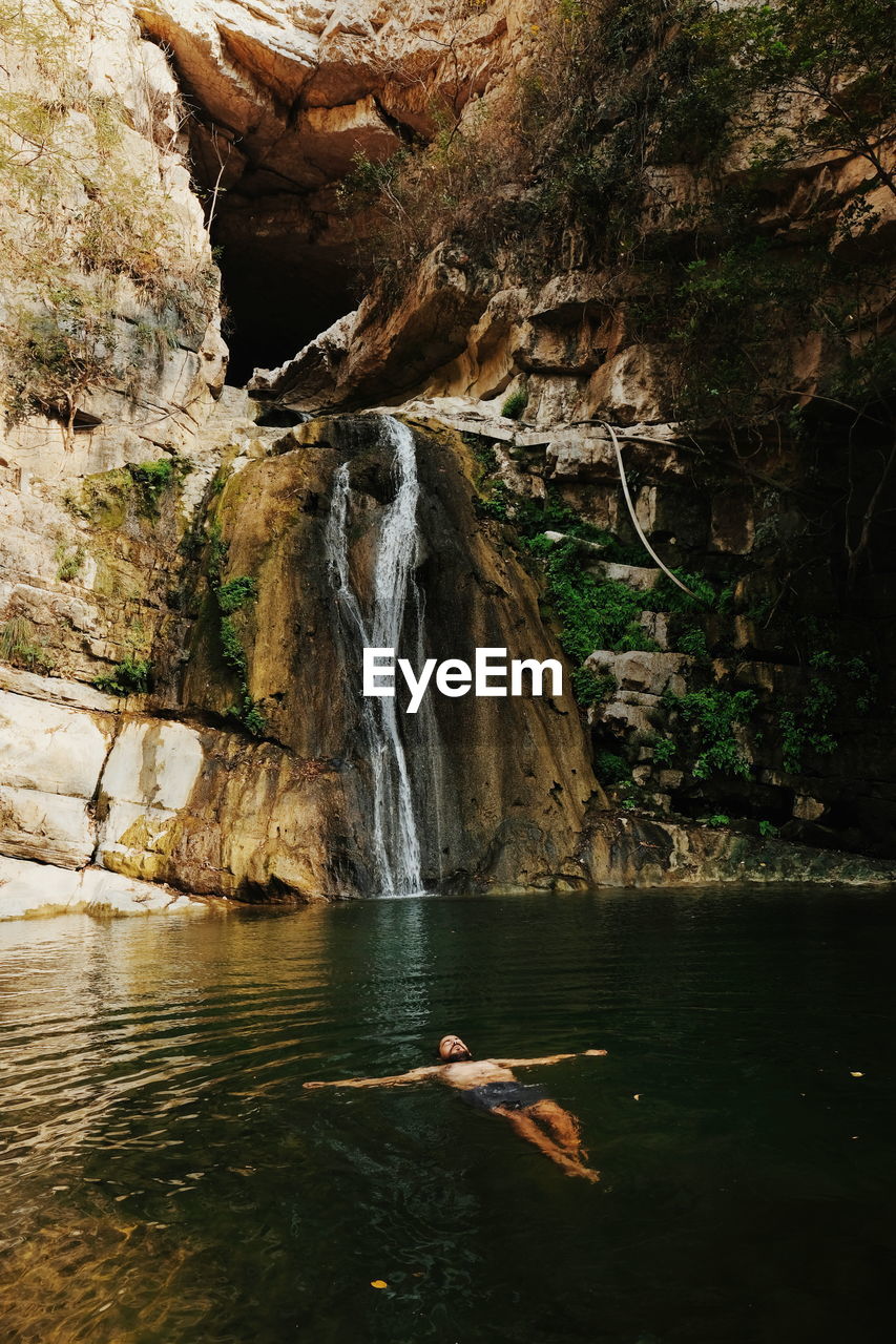 Man swimming in lake against waterfall