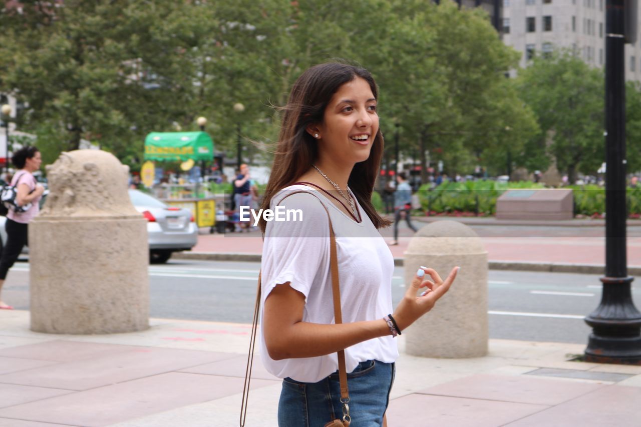 YOUNG WOMAN SMILING WHILE SITTING ON CITY IN PARK