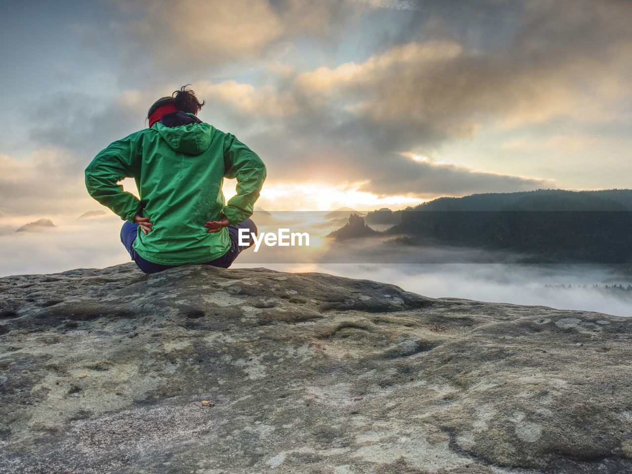 Beautiful girl in a hat and green jacket meditate while sitting on a stone in the mountains