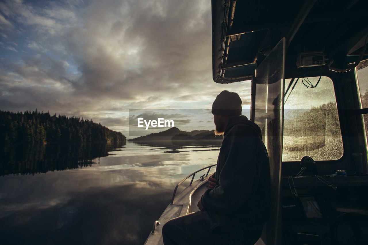 Man sitting in boat on lake against sky during sunset