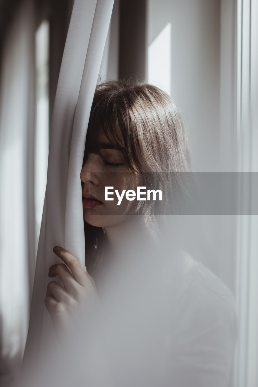 Worried woman standing by curtain