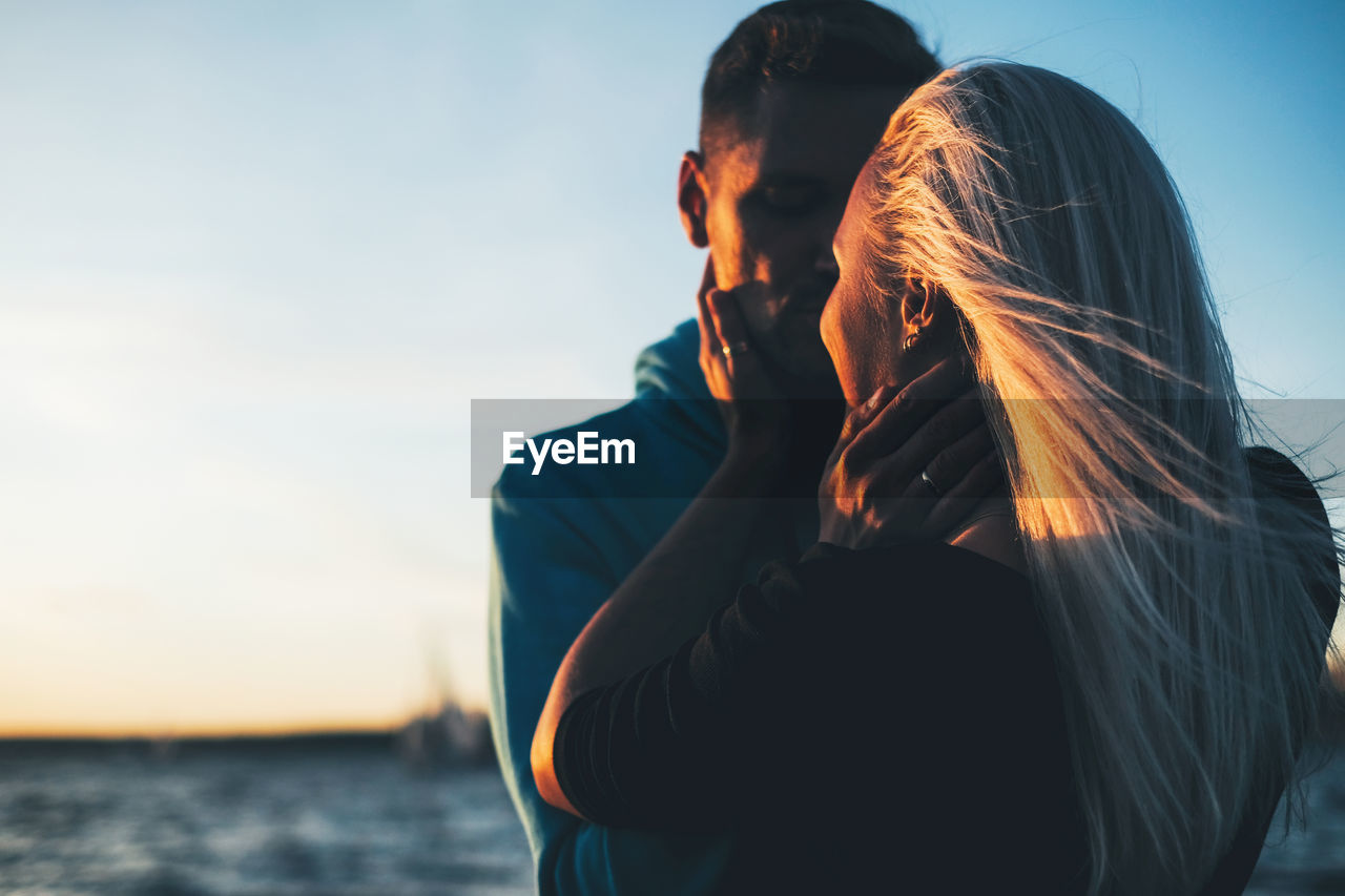 Close-up of couple embracing against blue sky